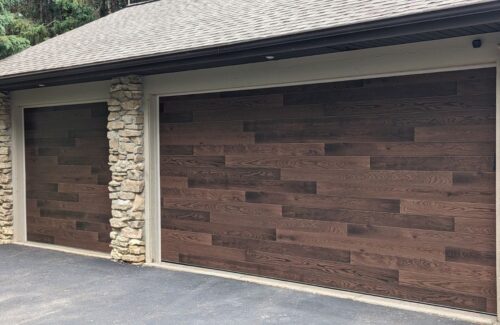 Suburban two-car garage with dark wood plank doors and stone pillars on a paved driveway.