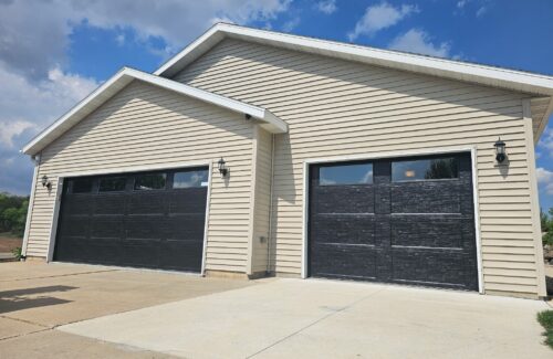 Two suburban garages with beige siding, dark textured doors, and exterior wall lamps.