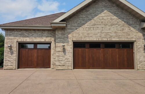 Light brown brick residential home exterior featuring two large wooden garage doors.