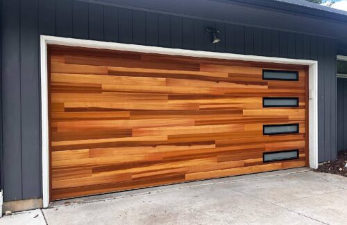 Modern garage door with horizontal wood panels and four right-side windows on a dark gray facade.