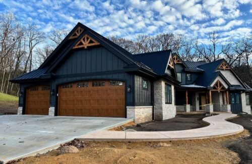 Modern dark gray house with peaked roofs, wooden garage doors, and a curved entrance walkway.