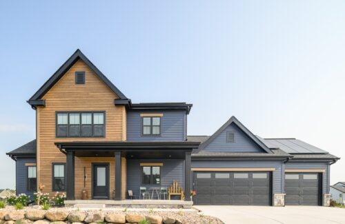 Modern two-story blue house with wood accents, a porch, a three-car garage, and a rock garden.